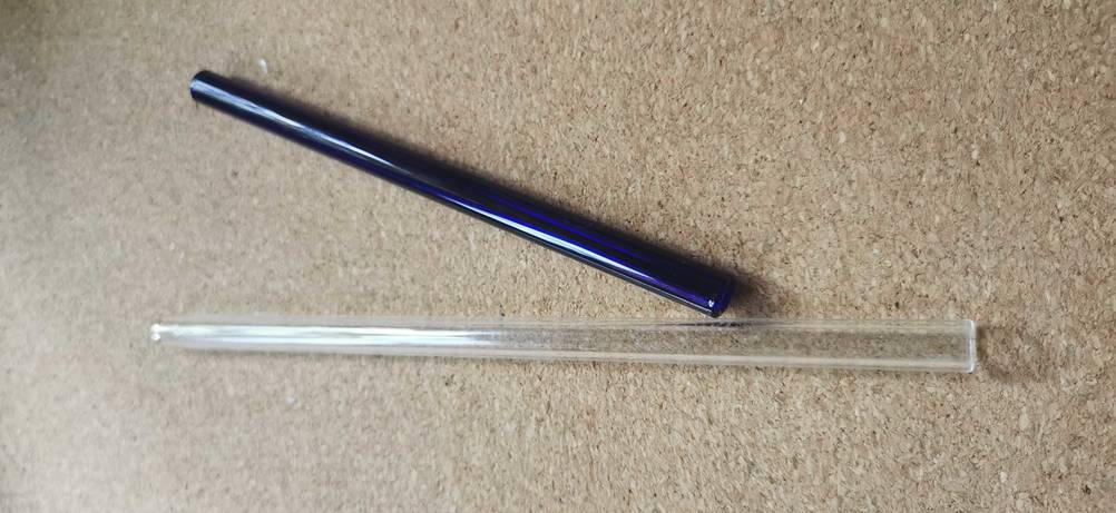 Glas-Strohhalme getestet: ein durchsichtiger Strohhalm liegend und ein blauer Strohhalm daneben patziert.