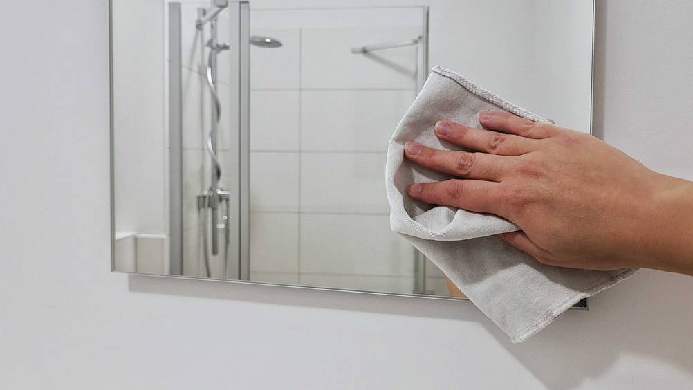 Badspiegel getestet: Eine Hand putzt mit einem Lappen den Spiegel.