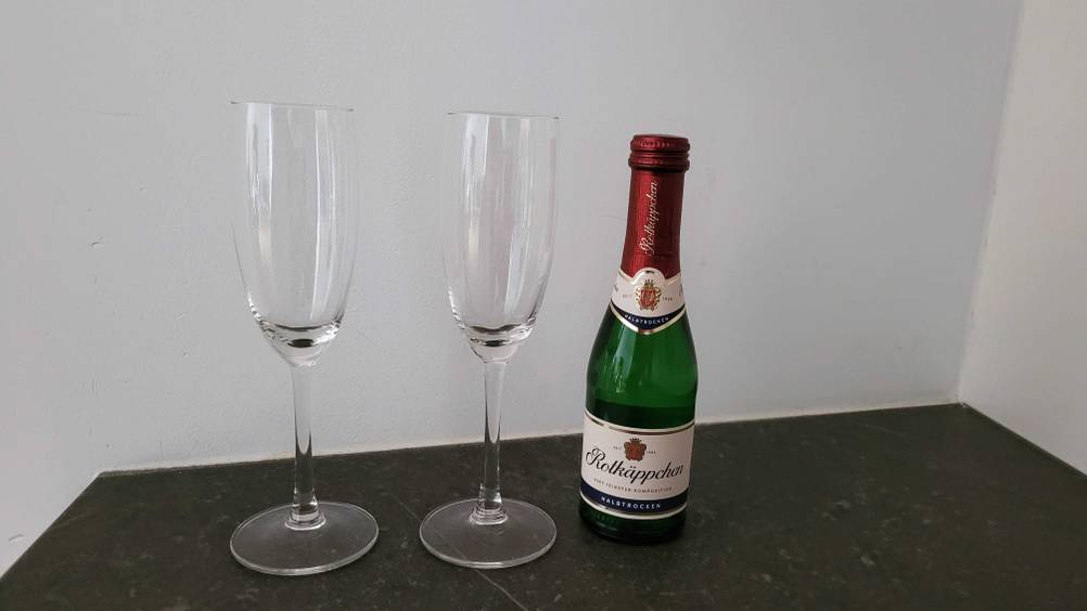 Sekt im Test: Auf einer dunklen Fläche stehen zwei Sektgläser und eine kleine Flasche Sekt