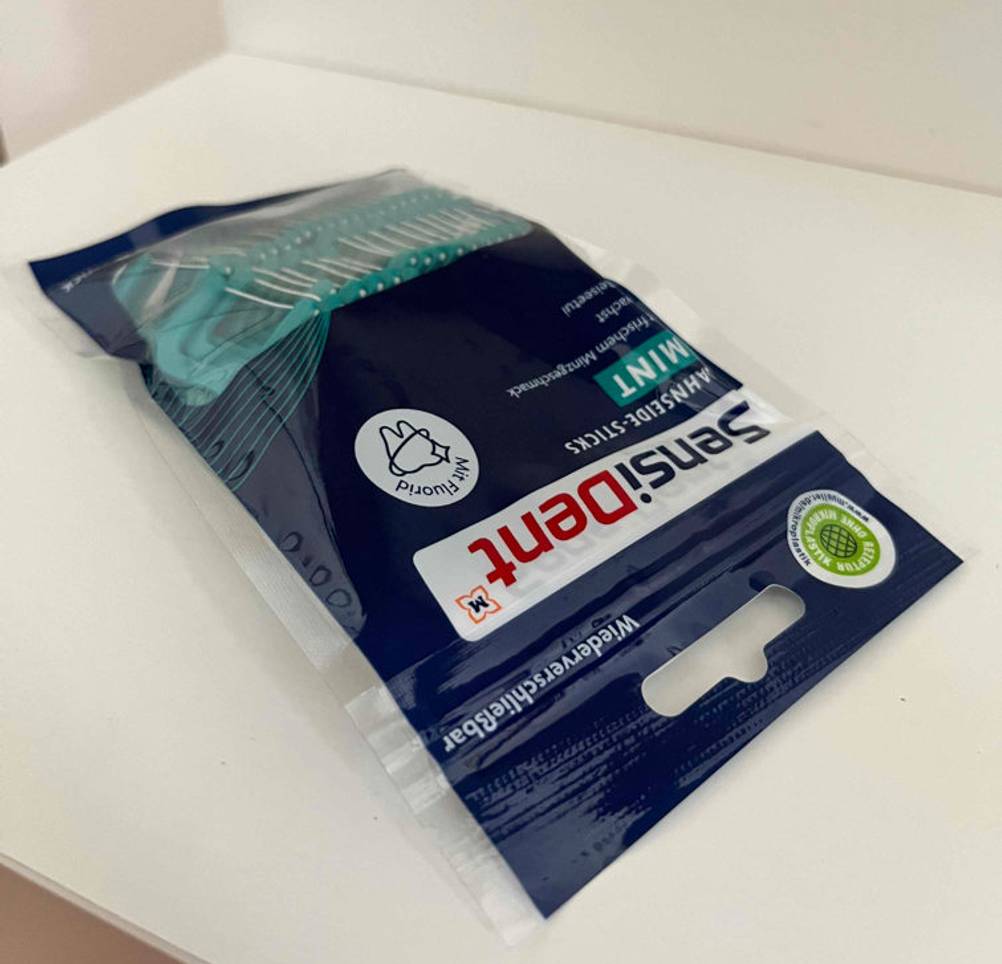 Zahnseidenhalter im Test: eine verschlossene Verpackung Zahnseidenhalter liegend auf einer weißen Fläche.