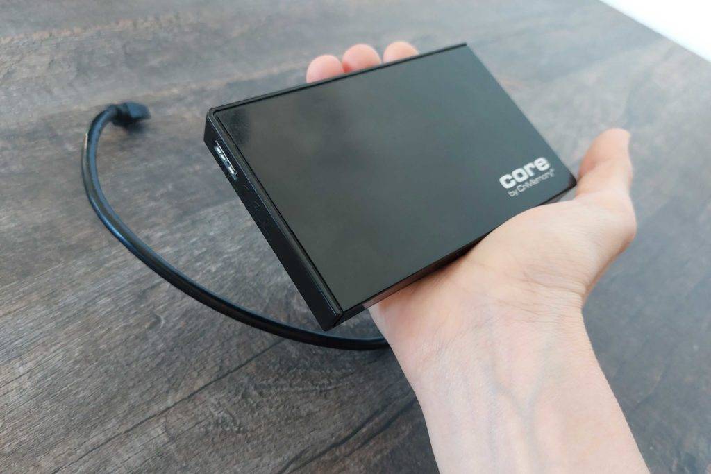 SSD Festplatte im Test: Eine Hand hält eine Festplatte über eine Holzoberfläche