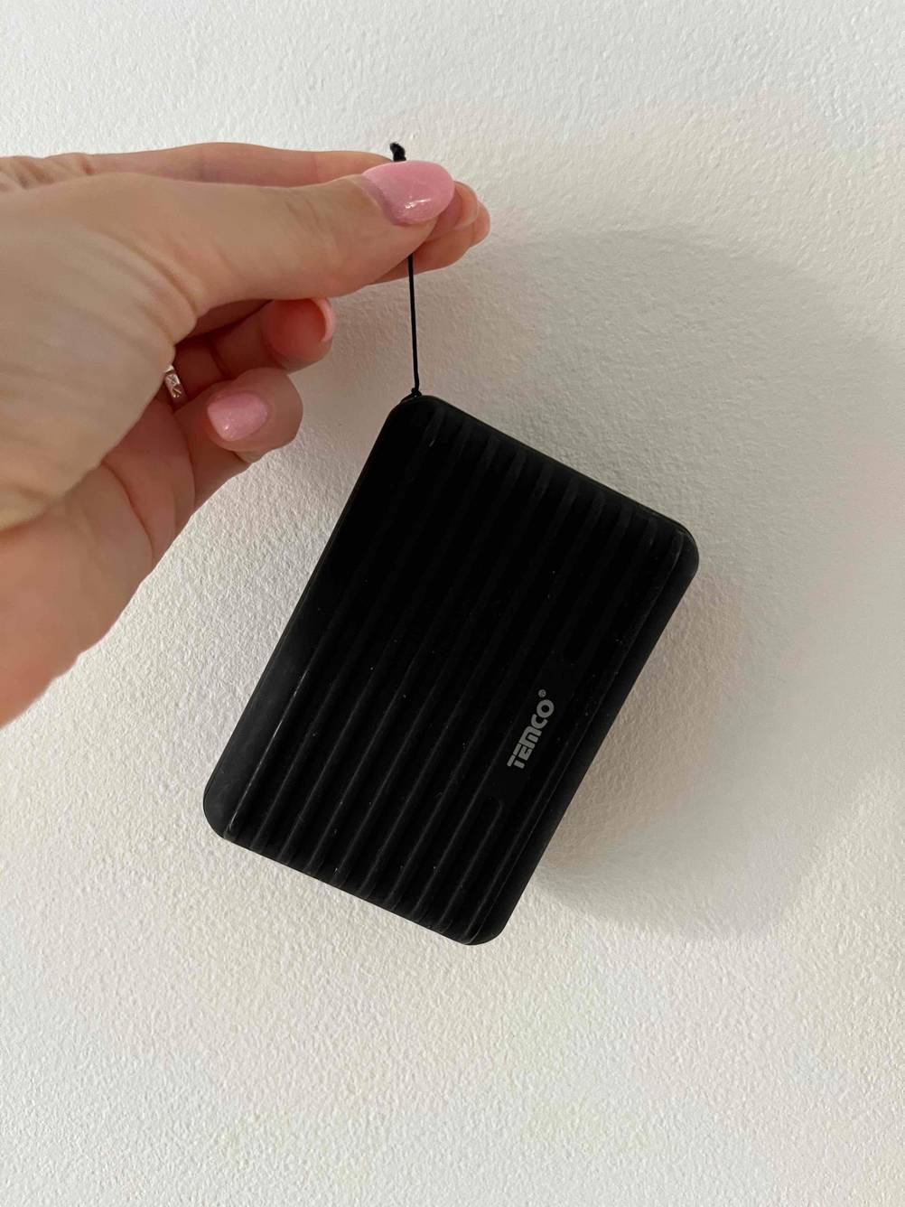 Powerbank-powerbank-10000mah-Test: Eine schwarze Powerbank wird an einer Schnur vor einer weißen Wand gehalten.