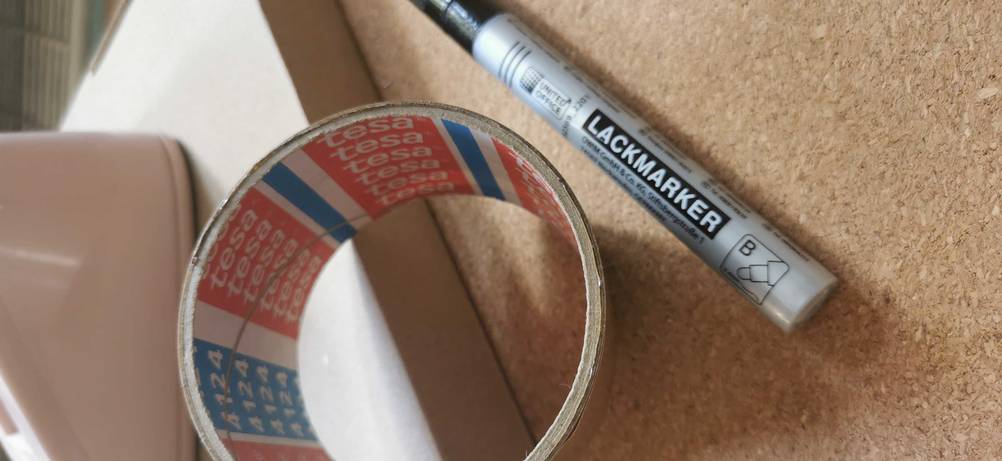 Parkettklebeband im Test: ein Lackstift in Schwarz liegt neben Parkettklebeband von Tesa.