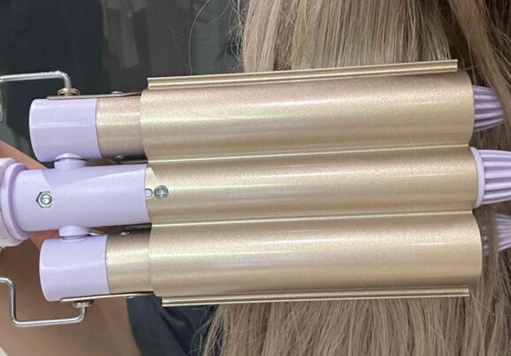 Ein getesteter Lockenstab mit 3 Stäben wird vor dem Haar gehalten.