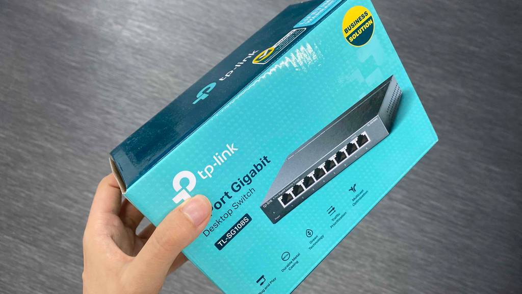 8-Port-Switch getestet: Eine Hand hält die Verpackung eines Switches vor grauen Hintergrund