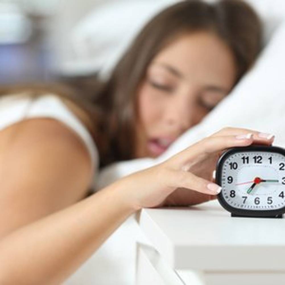 Frau, die den Alarm ihres Analog-Weckers am Morgen ausschaltet