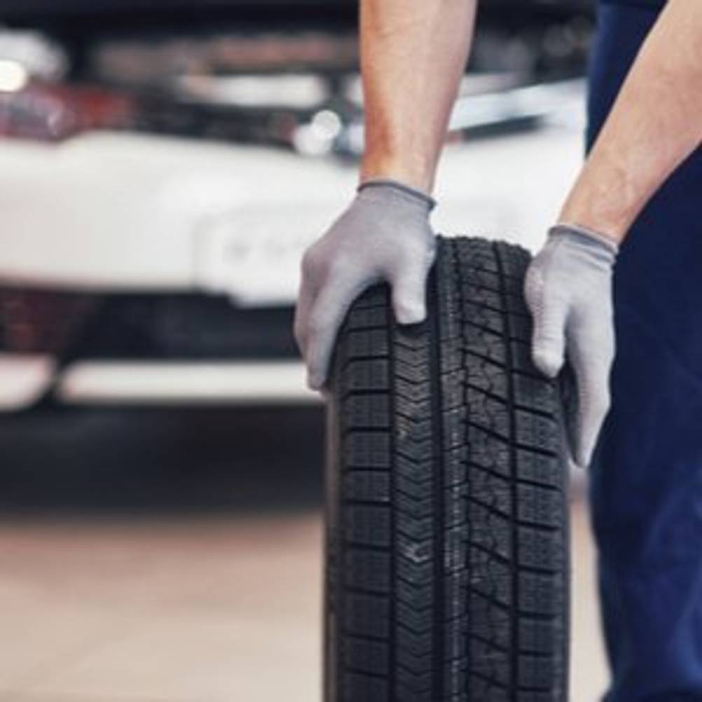 Mechaniker, der Reifen durch Werkstatt rollt und dabei Handschuhe trägt