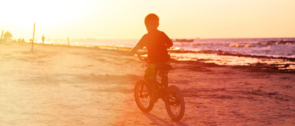 Junge auf Kinderfahrrad Richtung Sonnenuntergang am Strand