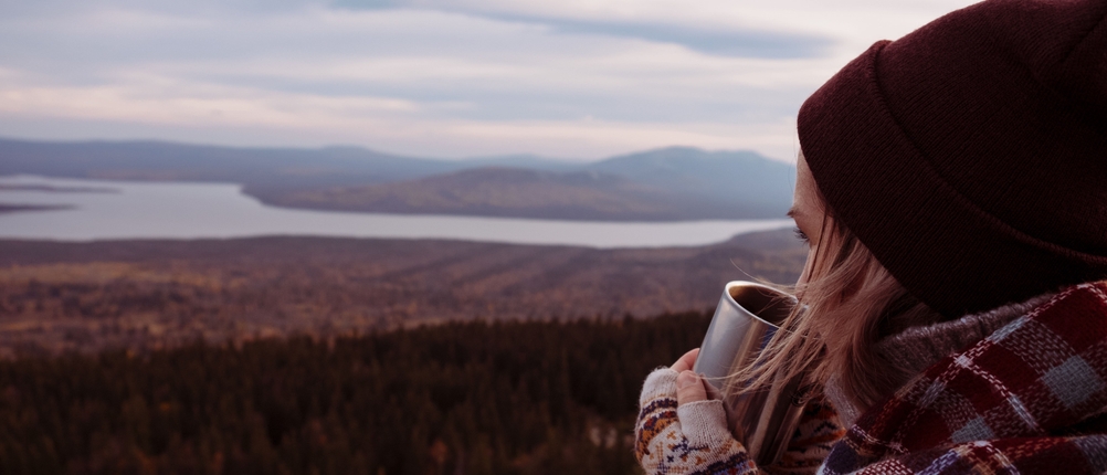 Frau trinkt Getränk mit Blick auf Landschaft mit See 