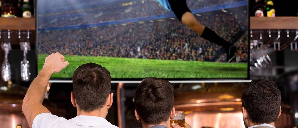 Beamer-Leinwand-Test: Drei Freunde schauen auf einer Leinwand ein Fußballspiel in einer Kneipe