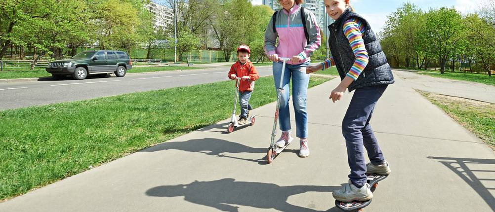 Waveboard-Test: eine Mutter mit zwei Kindern fahren mit dem Waveboard und Scootern auf einem asphaltierten Weg