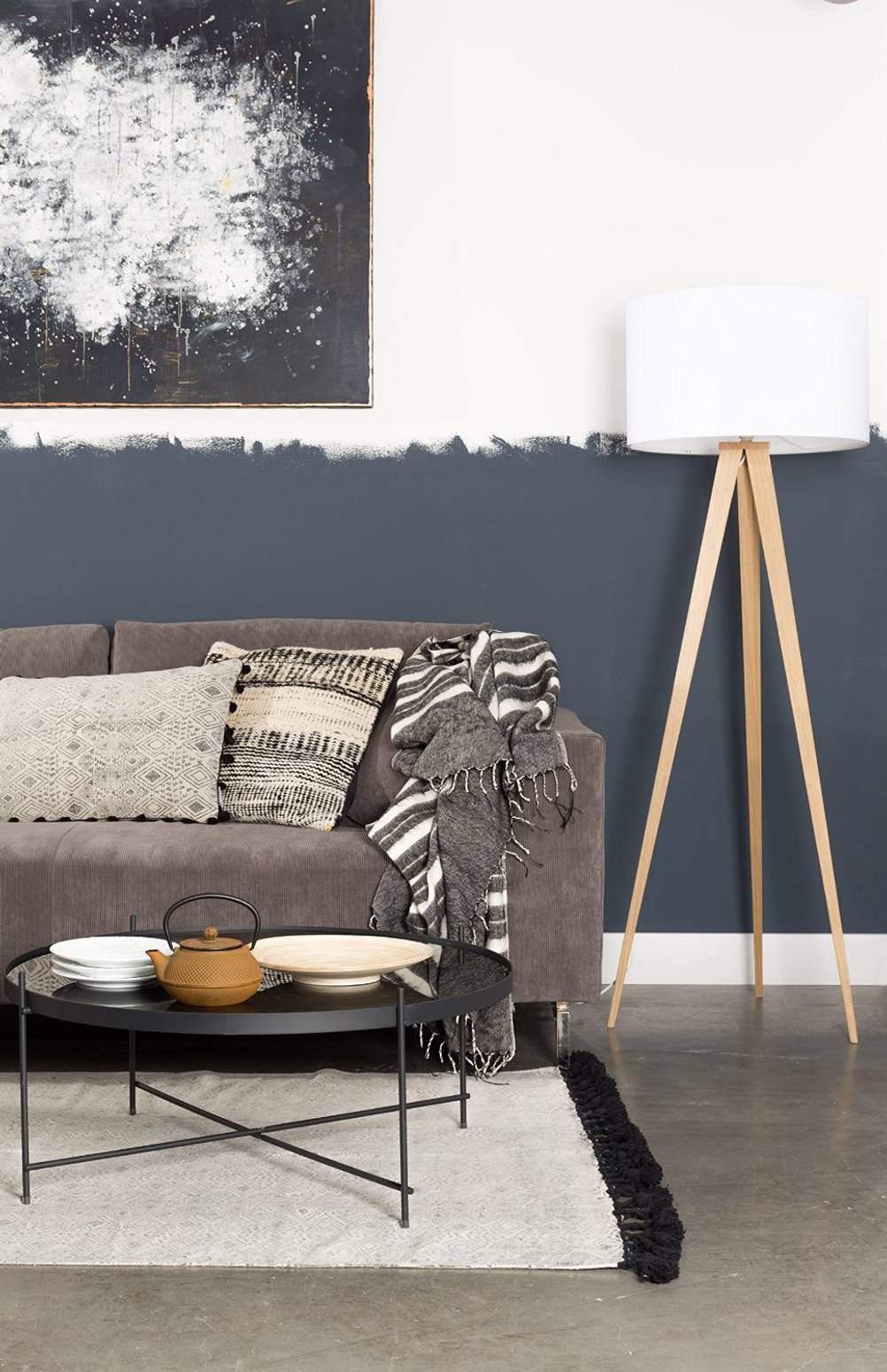 Wohnzimmer-Standlampe-Test: Zu sehen ist eine Stehlampe mit einem Holzfuß und einem weißen Lampenschirm rechts neben einem Sofa.