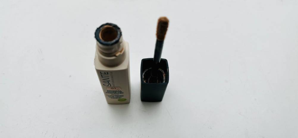 Eine Packung des Abdeckstifts im Test neben dem Aplikator auf einer hellen Fläche.