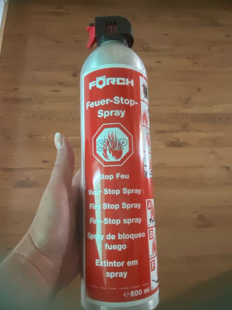 ABF-Feuerlöscher-Test: Eine Hand hält den 600-ml-Druckbehälter mit dem Feuer-Stop-Spray vor einer Holzfläche.