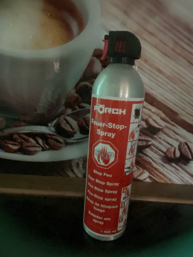 Der getestete ABF-Feuerlöscher inklusive Feuer-Stop-Spray in dem 600-ml-Druckbehälter liegt auf einem Frühstücksset im Kaffeebohnendesign.