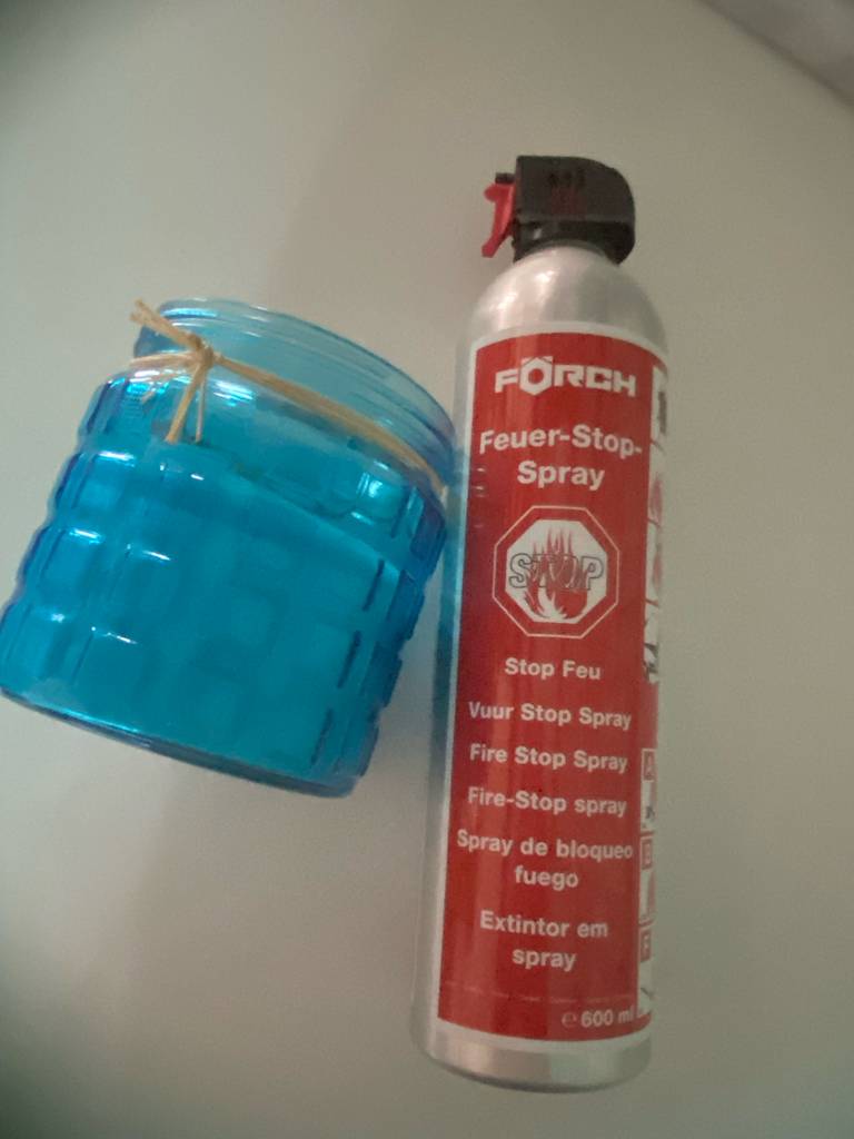 ABF-Feuerlöscher getestet. Ein Feuer-Stop-Spray in einem 600-ml-Druckbehälter liegt neben einem blauen Glasbehälter.