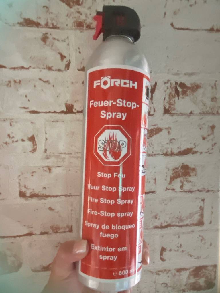 ABF-Feuerlöscher-Test. Ein Feuer-Stop-Spray in dem 600-ml-Druckbehälter wird von einer Hand vor einer weißen Ziegelwand gehalten.