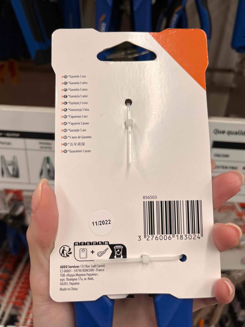 Rückseite einer Verpackung der getesteten Abisolierzange von einer Hand gehalten.