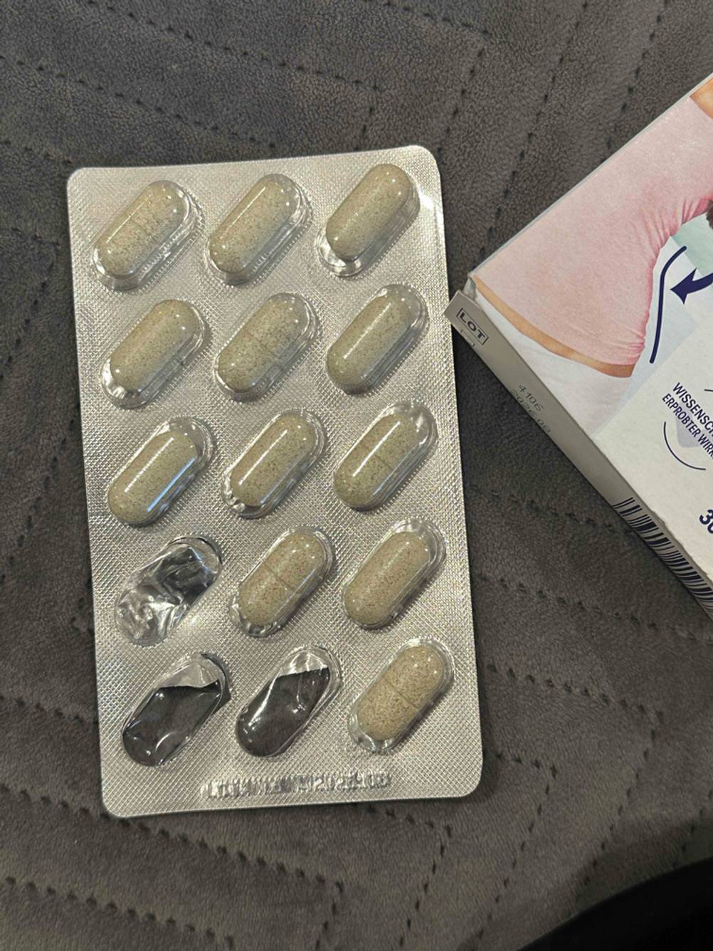 Getestet: Ein Tablettenblister der Abnehmpillen neben der Verpackung auf einer dunklen Fläche.
