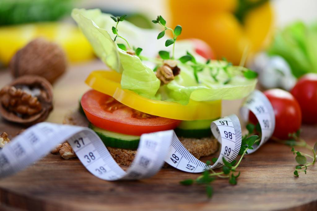 Ein mit Gemüse belegtes Brot und ein Maßband.