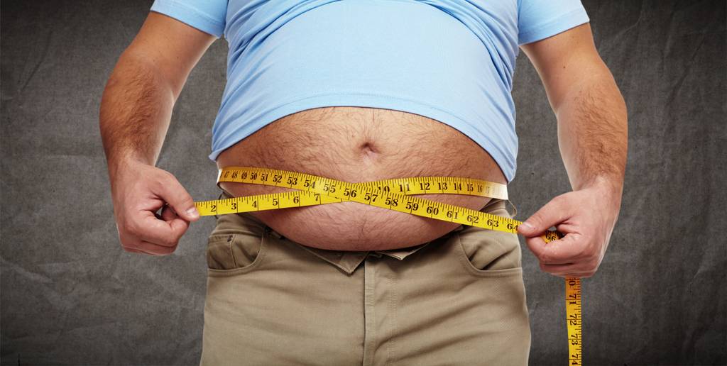 Ein Mann mit Bierbauch misst seinen Bauchumfang.
