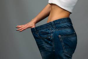 Abnehmprogramme getestet: eine schlanke Frau in einer zu großen Jeans