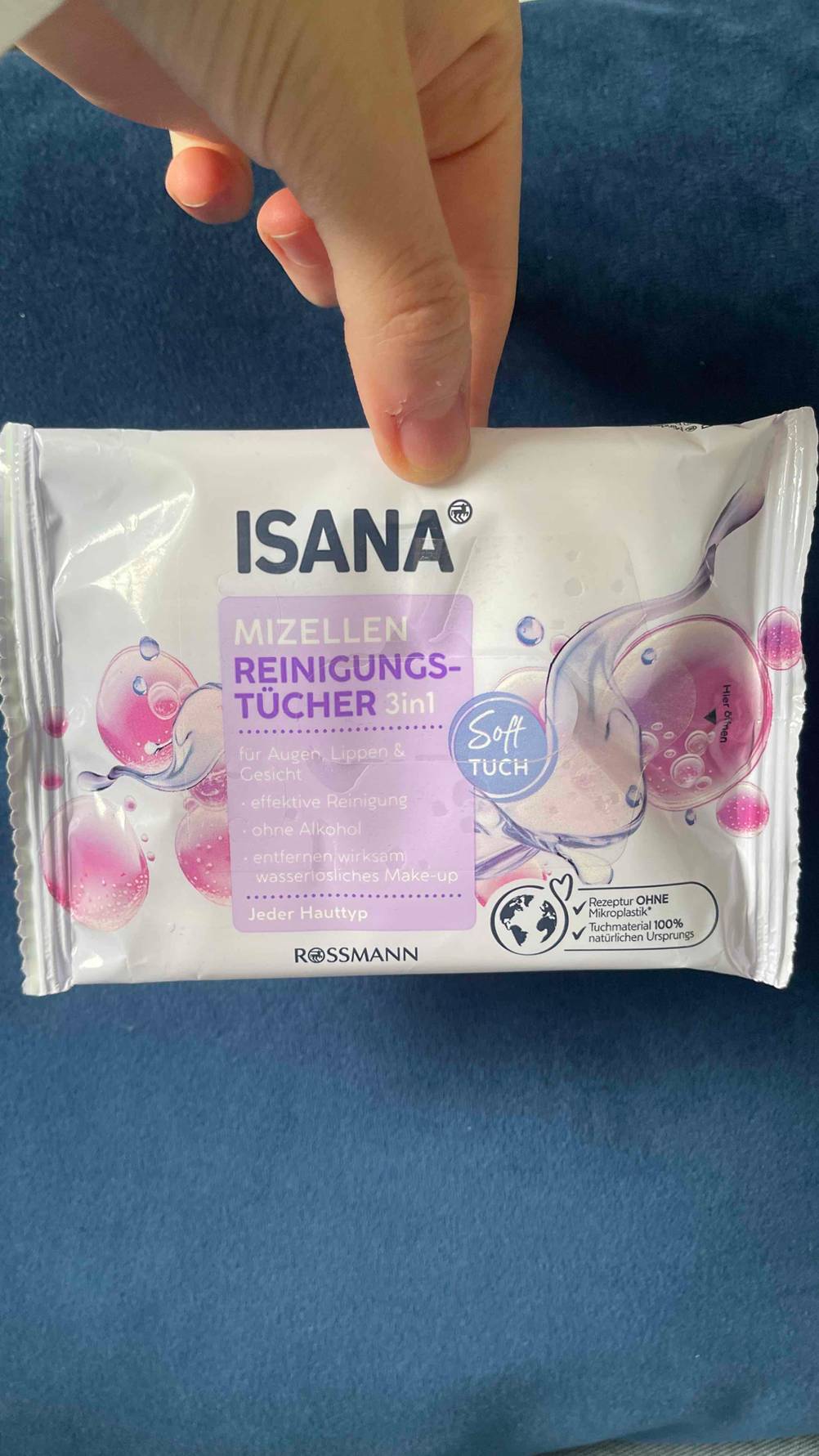 Ein Daumen hält eine Spenderpackung mit den getesteten Abschminktüchern über einer blauen Oberfläche.