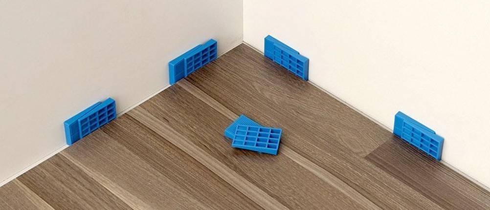Vinylboden liegt in einer Ecke und wird mit blauen Keilen von der Wand ferngehalten