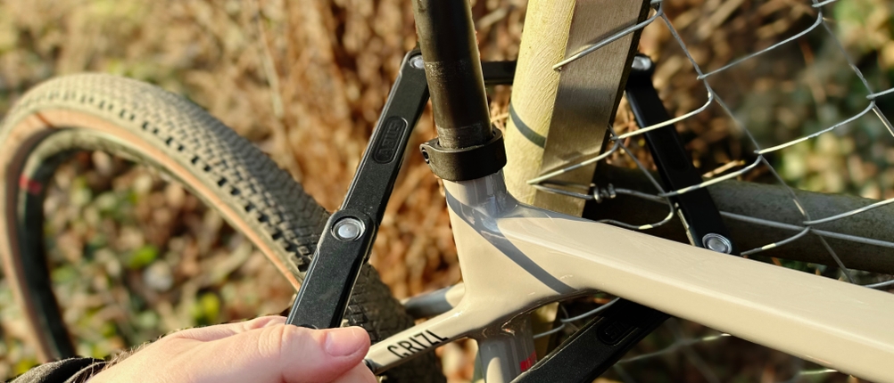 Das Abus-Faltschloss Bordo 6000K wird um den Rahmen und einen Zaunpfosten gelegt. Eine Hand hält das Schloss beim Anschließen.