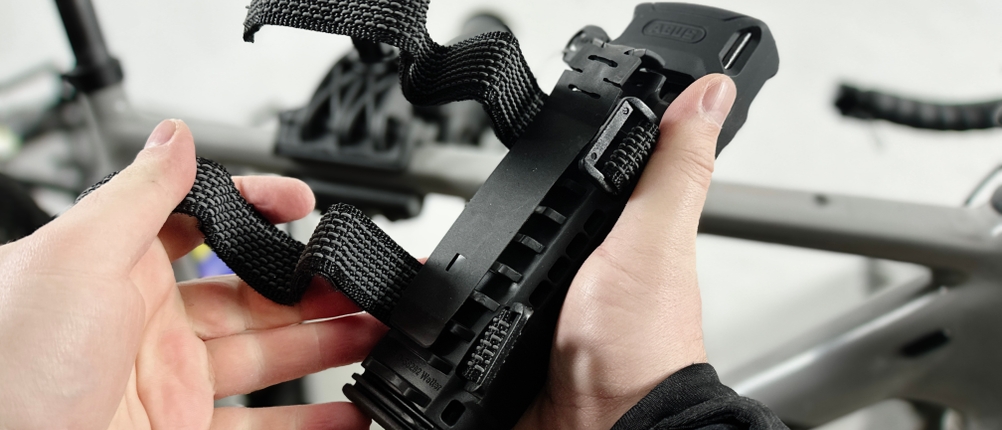 Das Abus Bordo 6000K ist in der Fahrradhalterung befestigt. Der Rahmen und die Befestigungsriemen sind sichtbar.