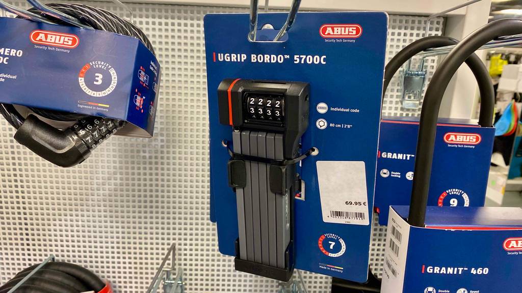 ABUS-Faltschlossä-Test: Ein ABUS-Faltschloss mit Zahlencode hängt in seiner blauen Verpackung an einem Verkaufsstand neben anderen ABUS-Schlössern.
