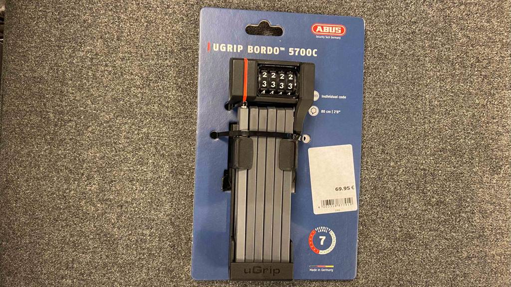 ABUS-Faltschloss im Test: Ein ABUS-Faltschloss mit Zahlencode liegt in seiner blauen Verpackung auf einem grauen Teppichboden.