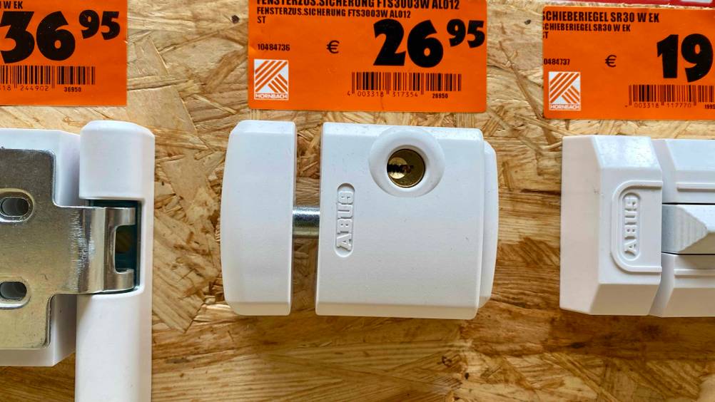 Im Test: Eine Fenstersicherung zwischen anderen Produkten an einem Holzbrett befestigt, darüber die Preisangabe.