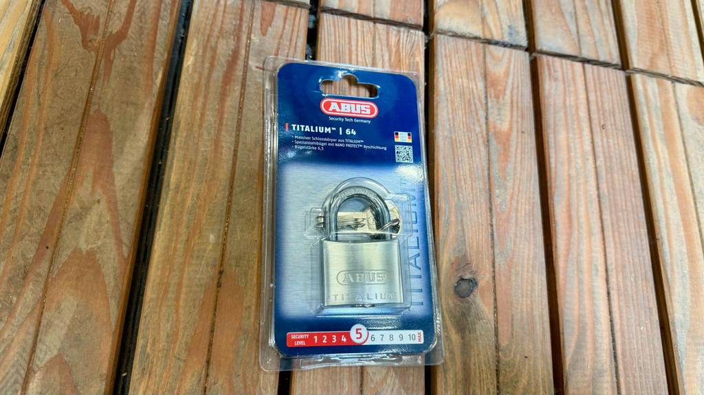 Abus-Vorhängeschloss im Test: Ein im Plastikblister verpacktes Schloss liegt auf einem Holzregal.