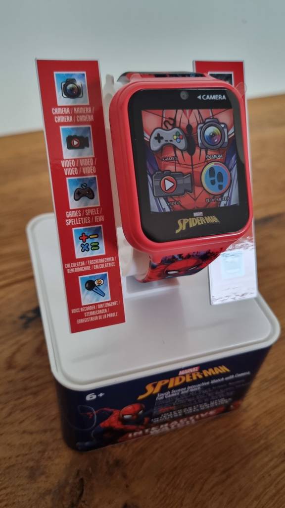 Eine Kinderuhr im Kasten mit Aufsteller zur Lagerung, daneben eine Auflistung der Features.