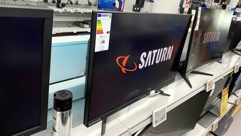 Ein getesteter Gaming Monitor mit 144Hz von schräg seitlich auf einem Verkaufsregal zwischen anderen Geräten und Preisangaben.