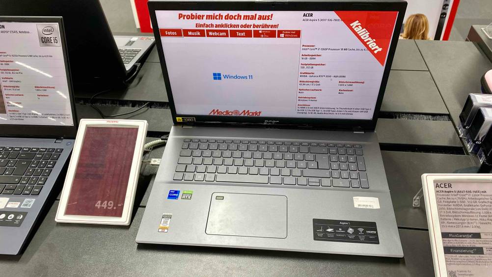 17-Zoll-Laptop getestet: Ein aufgeklapptes und angeschaltenes Gerät in einer Verkaufsausstellung mit Informationen und Preisschild.