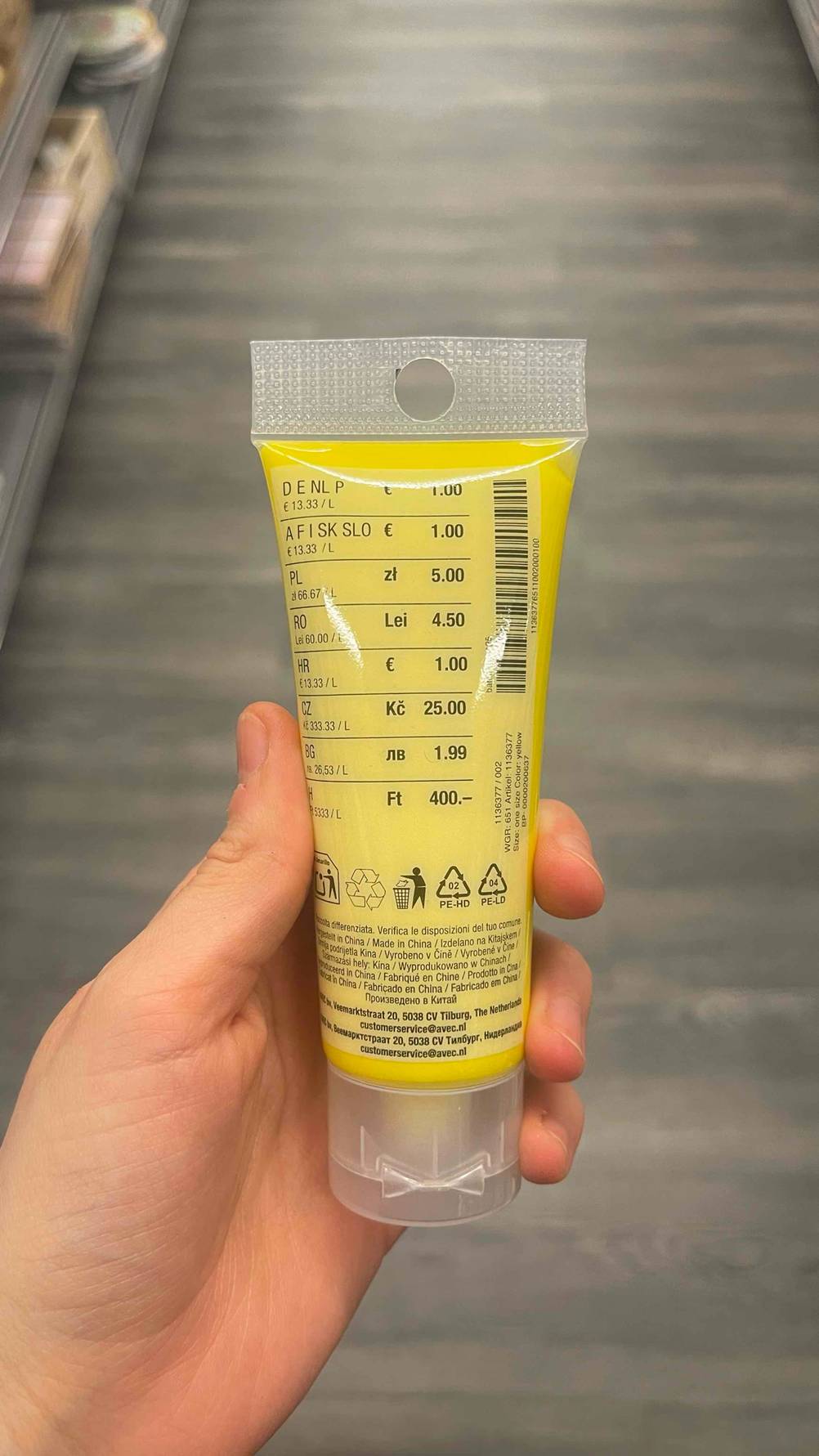 Eine Hand hält eine Tube getestete Acrylfarbe in gelb mit der Rückseite nach vorn.