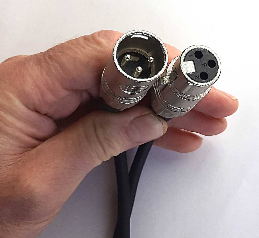 Eine Hand hält das schwarze, getestete Audiokabel mit zwei versilberten Steckern, der Fokus liegt auf den dreipoligen Eigenschaften, vor einem weißen Hintergrund.