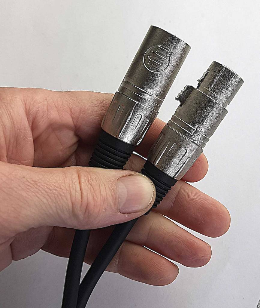 Audiokabel-Test: Eine Hand hält die beiden versilberten Stecker eines schwarzen Kabels vor einem weißen Hintergrund.
