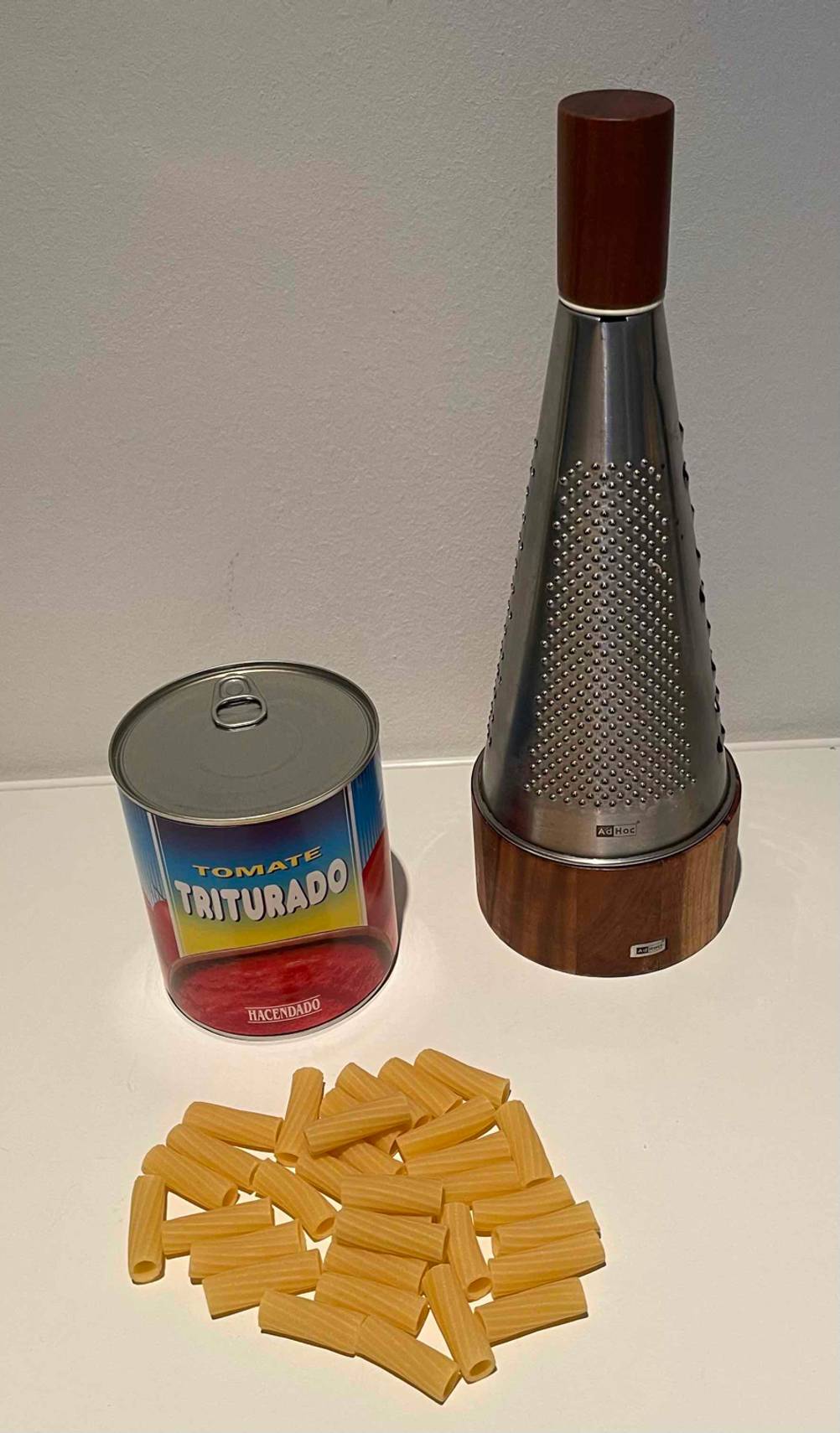 Eine Adhoc Parmesanreibe im Test befindet sich auf einer hellen Fläche zusammen mit Rigattoni sowie einer Dose Tomatensoße.