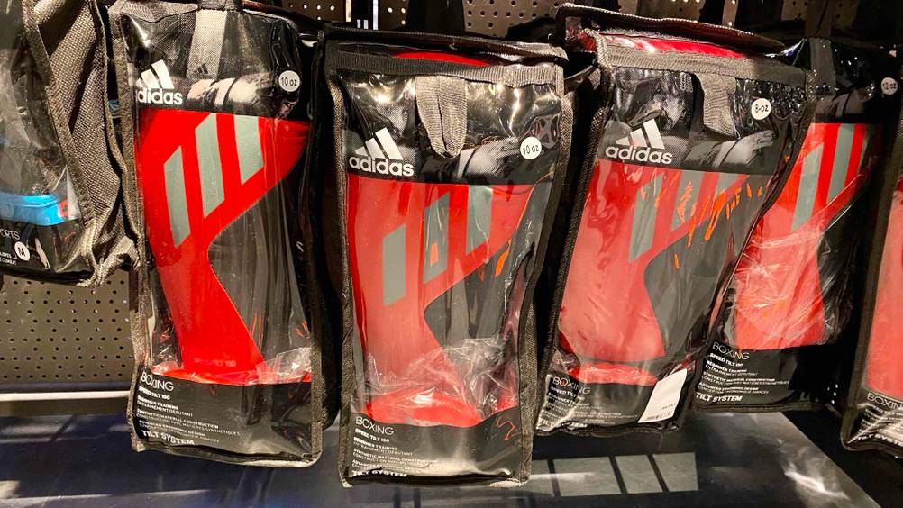 Mehrere schwarz-rote Adidas Boxhandschuhe im Test hängen in ihren schwarzen Verpackungen mit Sichtfenster an einem Verkaufsregal.