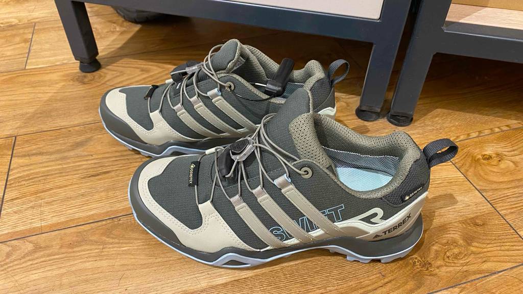 Seitenansicht von niedrigen beige-grauen getesteten Damen-Trekkingschuhen auf einem braunen Holzboden.