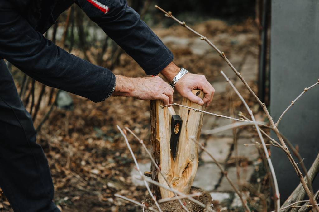 Handbeil im Test: Ein Mann drückt ein fast gespaltenes Holzstück auseinander, in dem ein Handbeil steckt.