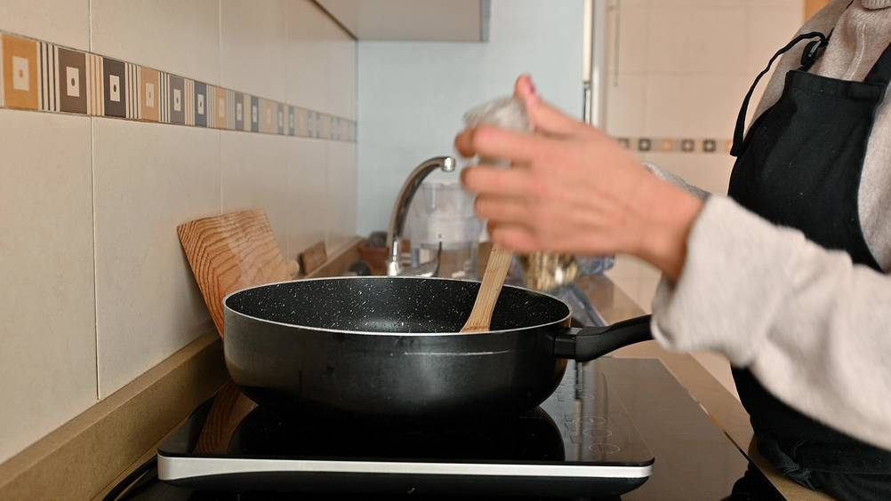 Caso-Induktionskochfeld im Test: Frau rührt in einer Pfanne mit einem Gewürz in der Hand. Kochfeld steht auf Einbau-Kochfeld.