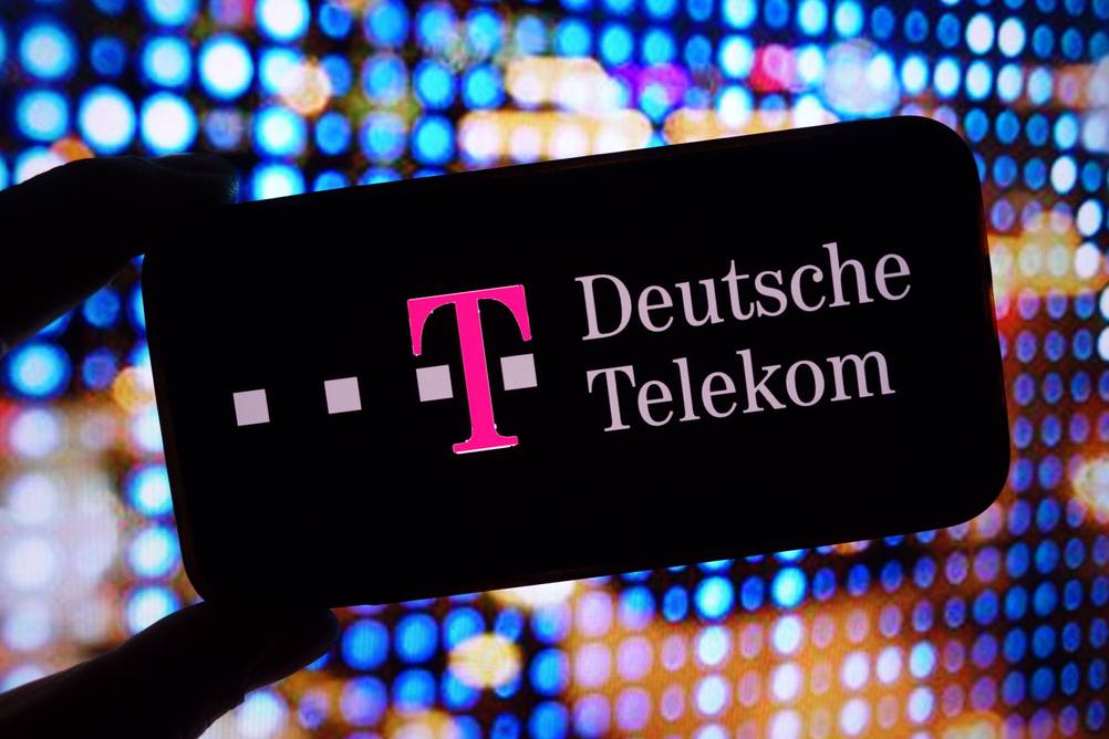 Telekom-Telefon im Test: Eine Hand hält ein Lable mit dem Logo der Deutschen Telekom ins Bild – im Hintergrund bunte Lichter.