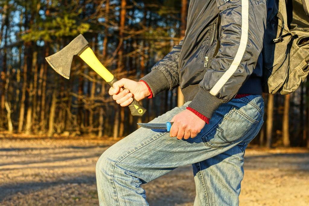 Handbeil im Test: Mann mit Jeans und Rucksack hält in einer Hand ein Messer und in der anderen ein Handbeil.