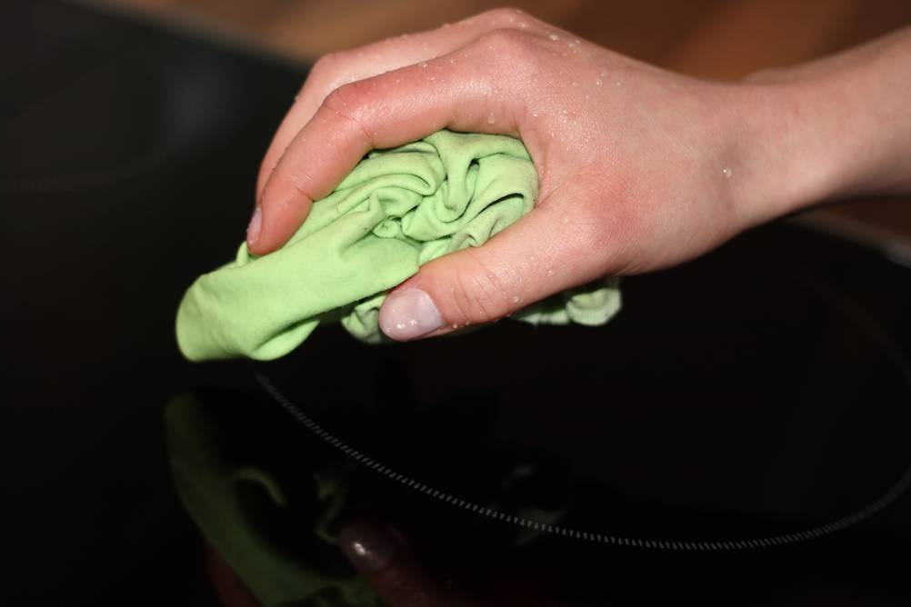 Teka-Kochfeld im Test: Eine Hand mit einem grünen, feuchten Lappen wischt über ein Glas-Kochfeld