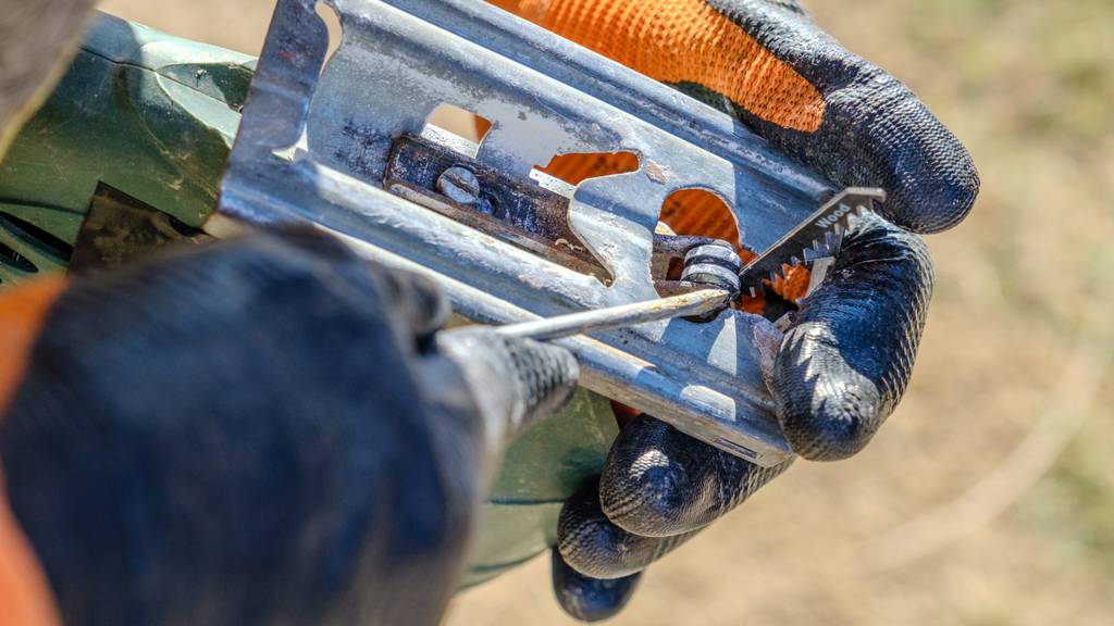 Stichsägeblatt im Test: Eine Person hält eine umgedrehte Stichsäge in Händen und hält einen Schraubendreher an die Halterung des Stichsägeblatts, das mit Wood beschriftet ist.