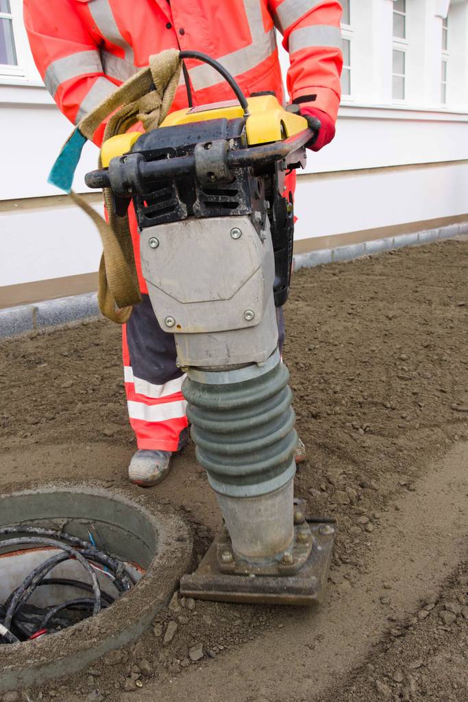 Vibrationsstampfer im Test: Ein Mann in Arbeitskleidung führt einen Vibrationsstampfer rund um einen Schachtring.